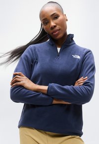 Μπλε ναυτικό φλις πουλόβερ με ψηλό γιακά, φερμουάρ μέχρι το στήθος και λογότυπο· διαθέτει μακριά μανίκια και υφή υφάσματος. Άνετη εφαρμογή.