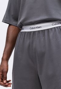 Set de lounge din bumbac gri, compus dintr-o bluză cu mânecă scurtă, cu o croială lejeră, și pantaloni cu talie elastică, accentuați de un logo alb Calvin Klein.