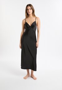 Vestido de satén negro con escote en V profundo, tirantes finos, cuerpo ajustado y falda fluida que cae hasta los tobillos. Textura suave.