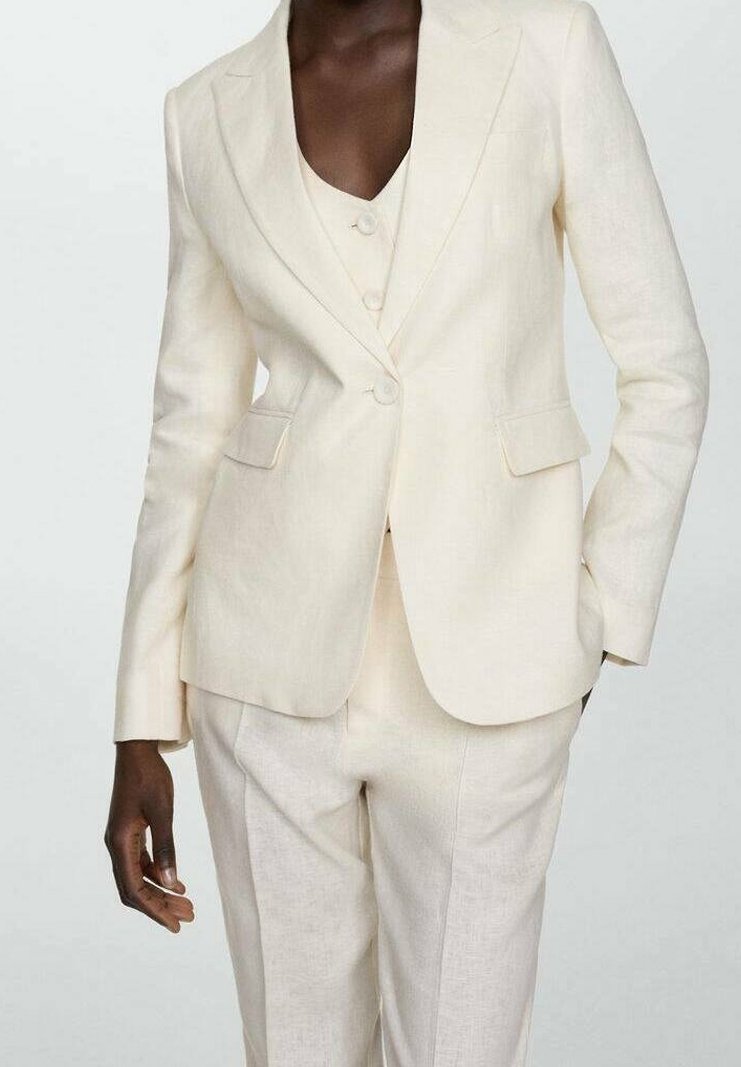 Costume en lin crème avec blazer ajusté présentant des revers en pointe et deux poches avant, associé à un gilet et un pantalon assortis.
