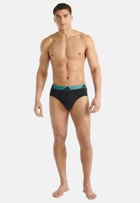 Czarne majtki z turkusowym paskiem w talii ozdobionym trzema paskami. Materiał wydaje się gładki i elastyczny, zaprojektowany dla wygody i dopasowania.