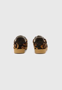 Un par de zapatillas de corte bajo con estampado de leopardo marrón y lengüetas de ante negro en suelas de goma beige, vistas desde la parte posterior.