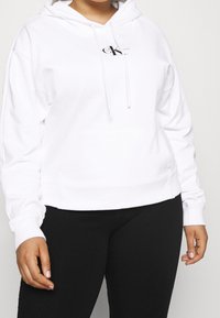 Felpa bianca con cappuccio e tasca frontale, caratterizzata da un piccolo logo nero sulla zona sinistra del petto. Tessuto morbido e vestibilità rilassata.