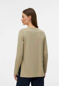Maglietta a maniche lunghe di colore marrone chiaro con scollo rotondo e lacci laterali. Realizzata in un tessuto morbido, presenta una vestibilità comoda e cuciture minime.