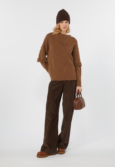 Maglione marrone a maglia con maniche frangiate e motivi geometrici, abbinato a pantaloni wide-leg in corduroy marroni e una borsa marrone.