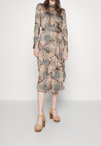 Lång skjortklänning i lätt tyg med flerfärgat rutmönster och guldkedjemotiv; inkluderar ett bälte i midjan och långa ärmar.