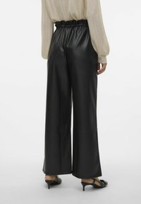 Zwarte, broek met wijde pijpen van een textuur, faux leren materiaal en een elastische, geraffineerde tailleband. Gestyled met zwarte haksandalen.