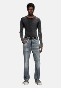 Chemise à manches longues, gris foncé, ajustée avec des coutures contrastées ; associée à un jean bleu délavé et des baskets grises avec des accents rouges.