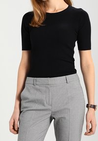 Sort ribbet t-shirt med korte ærmer parret med grå ternede højtaljede bukser med en skræddersyet pasform og en glat tekstur.