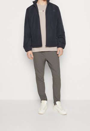 Navy puffer jacket with a high collar, beige t-shirt with text, gray striped pants, and white sneakers with yellow accents.