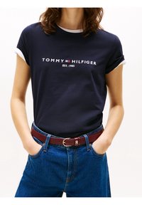 Námořnické bavlněné tričko s bílými manžetami, s logem "TOMMY HILFIGER EST. 1985". V kombinaci s modrými džínami a burgundským opaskem.