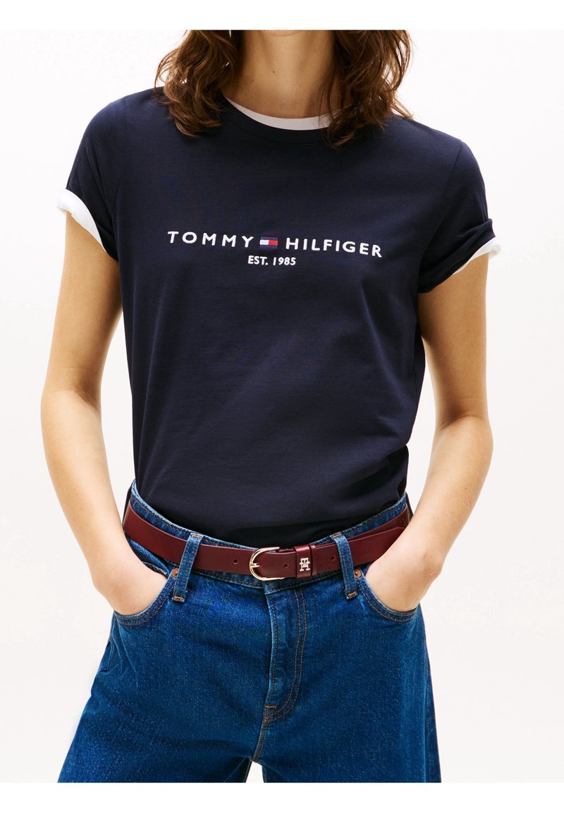 Námořnické bavlněné tričko s bílými manžetami, s logem "TOMMY HILFIGER EST. 1985". V kombinaci s modrými džínami a burgundským opaskem.