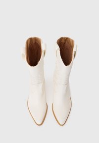 Bottes blanches à la cheville avec un bout pointu et des surpiqûres sur la tige. Matériau en cuir lisse et doublure intérieure marron.