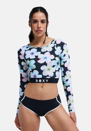 Rash guard à manches longues à fleurs en noir avec des fleurs roses, bleues et blanches. Présente une coupe ajustée et un logo Roxy sur la ceinture.