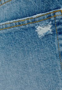 Ljusblå denimtyg med en synlig söm och en liten fransig fläck, som visar en sliten textur och en avslappnad design.