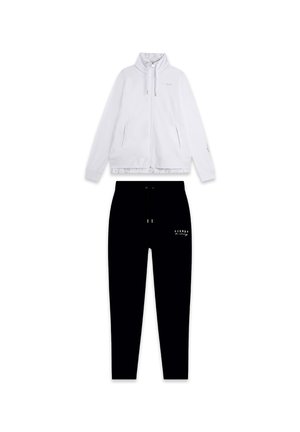 Giacca bianca con zip e colletto alto, decorata con accenti dorati, abbinata a pantaloni della tuta neri con logo. Il materiale sembra morbido e strutturato.