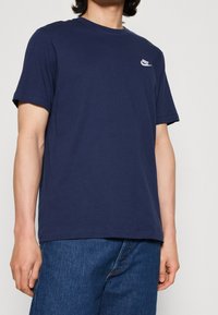 Marinblå bomull t-shirt med rund hals, kort ärm och en liten vit Nike-logotyp på övre vänstra bröstet. Slät textur.