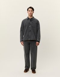 Svart denimskjorte med knapper foran, brystlomme og krage-design. Sammen med løse svarte denimbukser. Brune sko.