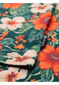 Květinová košile se zeleným pozadím, na kterém jsou velké oranžové a bílé hibiscus květy, listové vzory a černá značka.