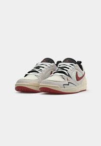 Sneaker con una parte superiore in rete bianca, accenti in suede grigio, lacci neri, logo rosso e una suola in gomma rossa. Presenta dettagli testurizzati e design a contrasto.