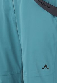 Turkosa vandringsbyxor gjorda av lättviktsmaterial, med en jämn yta, svarta logodetaljer nedanför benet och en kontrasterande midja.