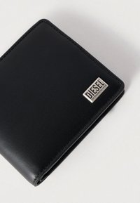 Μαύρο δίπτυχο πορτοφόλι από δέρμα με υφή στην επιφάνεια. Διαθέτει ασημένια πλακέτα με το λογότυπο DIESEL και ραφές αντίθετου χρώματος στα άκρα.