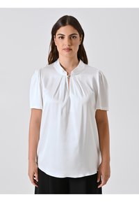 Blusa bianca a maniche corte con colletto alla cinese e frontale plissettato, dotata di una piccola chiusura decorativa. Tessuto liscio, vestibilità leggermente ampia.