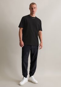 Čierne bavlnené tričko s krátkymi rukávmi, skombinované s tmavomodrými joggingovými nohavicami s elastickými manžetami, doplnené o biele tenisky. Jednoduché dizajnové detaily.