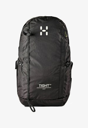 Mochila compacta negra con correas verticales, hebillas laterales y texto y logo blancos "TIGHT LIGHT" en el panel frontal.