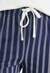 Calças de algodão azul-marinho com riscas brancas verticais, com cintura elástica e cordão para ajuste.