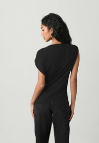 Sort t-shirt med korte, rullede ærmer og en afslappet pasform. Fremstillet af blødt stof, med en buet kant og en glat tekstur.