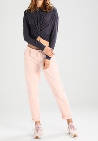 Ciemnoszara, długorękawowa, związana crop top w połączeniu z jasnoróżowymi, podwiniętymi dżinsami i beżowymi sneakerami z różowymi akcentami. Minimalistyczny design.