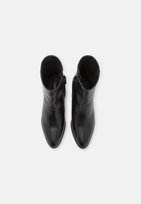 Bottes cheville en cuir noir avec bouts pointus, dotées d'une fermeture éclair latérale et d'une texture lisse, conçues pour une silhouette élégante.