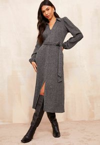 Grau gestreiftes Strickkleid mit langen Ärmeln, V-Ausschnitt, tailliertem Bund und seitlichem Schlitz, kombiniert mit knielangen schwarzen Lederstiefeln.