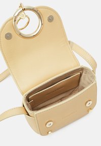 Borsa a tracolla in pelle di un beige chiaro con un accento circolare in oro, dotata di un compartimento aperto e di uno spazio per le carte più piccolo all'interno.