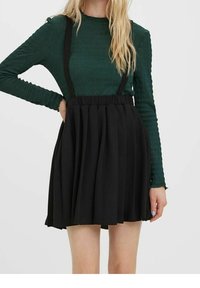 Zwarte geplooide rok met verstelbare zwarte bretels, gecombineerd met een groen, lang mouwtop met textuur. De stof lijkt soepel en licht van gewicht te zijn.