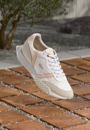 White athletic shoe with light peach accents, textured side panels, and a smooth toe cap, featuring a patterned rubber sole.
