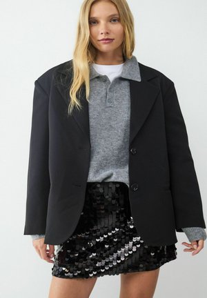 Blazer noir oversize, pull col montant gris et mini-jupe en sequins noirs brillants. Le blazer présente deux boutons et un design structuré.