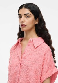 Roze shirt van een gestructureerde, fuzzy stof met een kraag en korte mouwen, gedetailleerd met knopen aan de voorkant.
