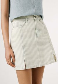 Gestreepte denim mini-jurk in lichtgroen en wit, met zijsplitten, voorzakken en metalen knoophardware.