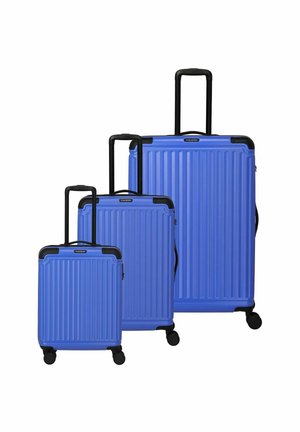 Trois valises rigides bleues avec un design à rainures verticales, des poignées noires et chacune sur quatre roues. Tailles variées allant de petite à grande.