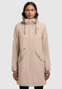 Beige vattentät jacka med hög krage, dragsko på huva, framsida med dragkedja och två stora fickor. Slät textur med en minimalistisk design.