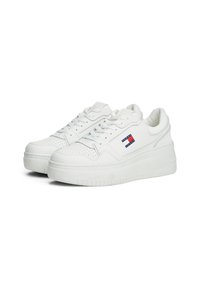 Baskets blanches avec une tige en cuir texturé, des accents perforés et une semelle en caoutchouc épaisse. Présente un petit logo rouge, blanc et bleu.
