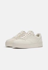 Adidași albi din piele cu vârf rotund, design cu șireturi, detalii perforate și talpă groasă pentru un plus de înălțime. Textură fină pe toată suprafața.