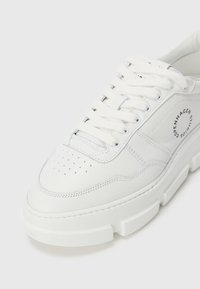 Hvit lær sneakers med tykk såle, perforert tå, snøring og sirkulært "Copenhagen Studios"-logo på sidepanelet.