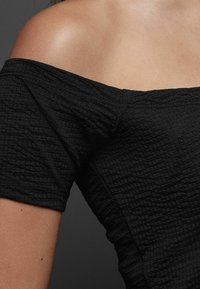 Top nero scollo scoperto realizzato in tessuto testurizzato, con un design a coste e una vestibilità aderente, che mette in risalto il décolleté e le spalle.