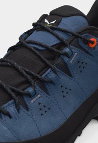 Μπλε και μαύρο πεζοπορικό παπούτσι με κορδόνια μαύρου και μπλε σχεδίου, πορτοκαλί οφθαλμό και υφή σόλας με λαβή, κοντινή λήψη.