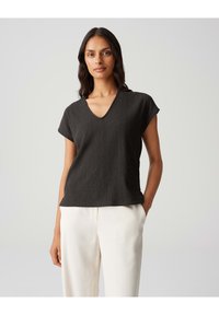 Top nero a maniche corte con scollatura a V, realizzato in tessuto testurizzato. Tagliato per adattarsi in modo morbido, abbinato a pantaloni di colore chiaro.