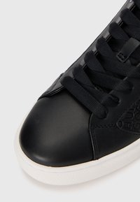 Zwarte leren sneakers met een ronde neus, platte veters, een witte rubberen zool en een gegraveerd logo op de zijkant. Textuurstof op de tong.