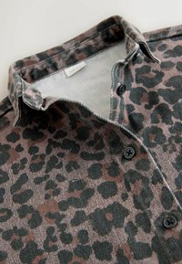 Košulja s printom leopardove kože s crnim gumbima i špicastim ovratnikom, ravno položena na bijeloj podlozi.